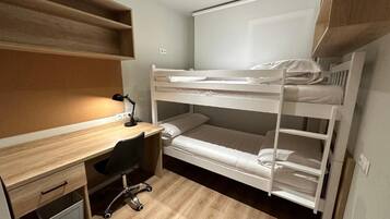 Una cama individual superpuesta con escritorio, silla, un estante pequeño y una ventana.