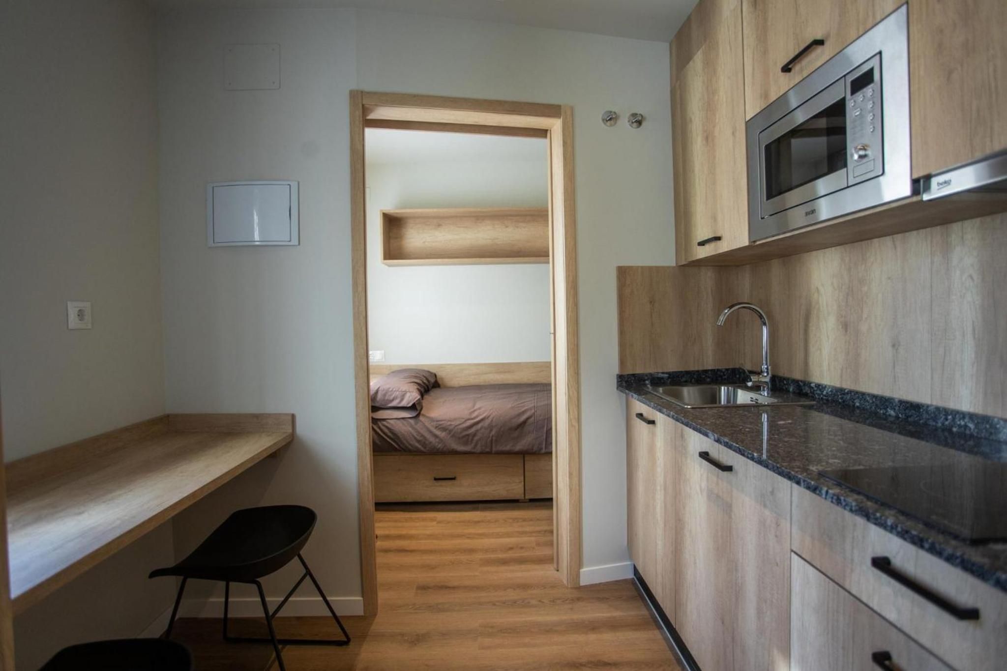 Una cocina compacta con microondas integrado, un lavamanos y armarios de madera.