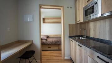 Una cocina compacta con microondas integrado, un lavamanos y armarios de madera.