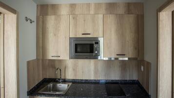 Una cocina compacta con armarios de madera, un microondas integrado, un lavamanos y una hornilla.