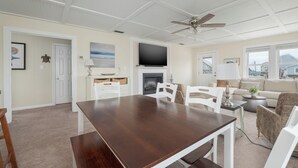 Un vaste espace de vie comprenant une table à manger, des chaises blanches, une cheminée et un téléviseur fixé au mur.
