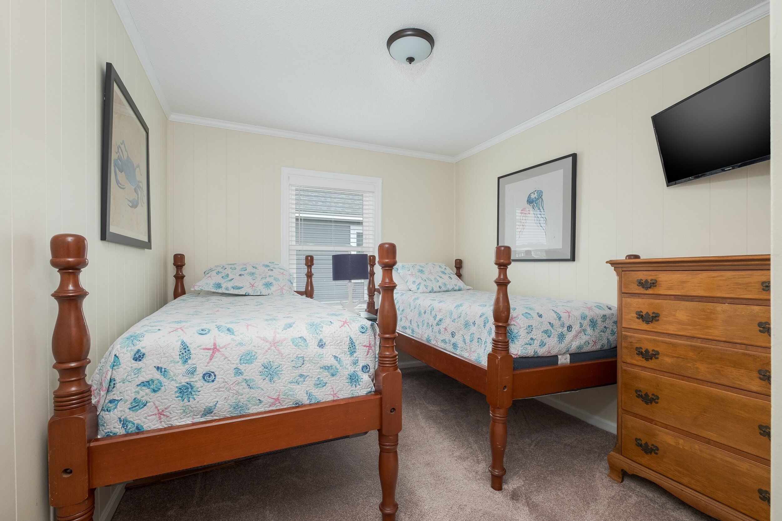 Une chambre à coucher avec deux lits en bois, une commode, un téléviseur à écran plat et des œuvres d’art encadrées accrochées aux murs.