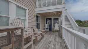 Une terrasse en bois avec des fauteuils Adirondack, un espace couvert et un escalier menant à un deuxième étage.