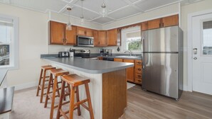 Une cuisine moderne avec des meubles en bois, un réfrigérateur en acier inoxydable et un îlot central doté de tabourets de bar.