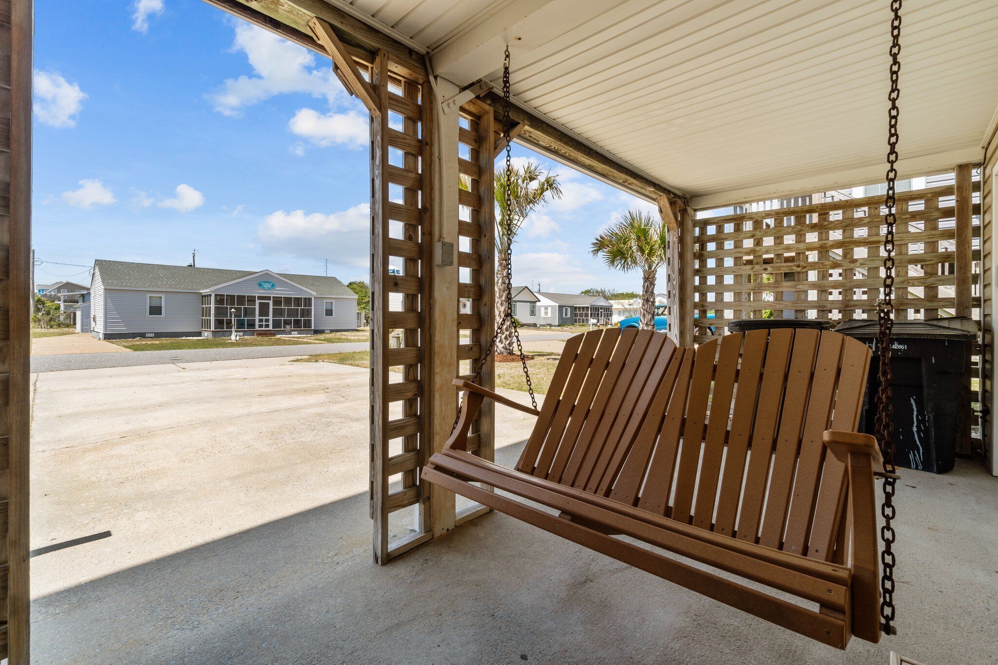 A wooden swing chair in a covered outdoor area with a view of houses and a clear sky.