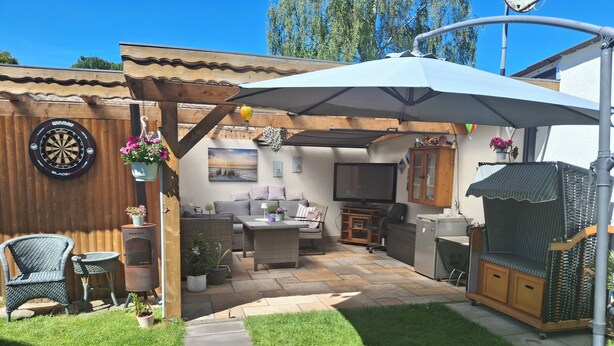 Eine Terrasse mit Essplatz, Dartscheibe und Fernseher.