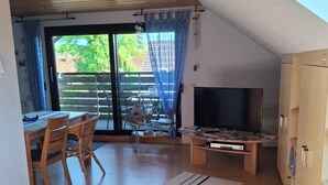 Ein modernes Wohnzimmer mit Holzboden, einem Essbereich mit Tisch und Stühlen, einem Fernseher und einem Bücherregal.
