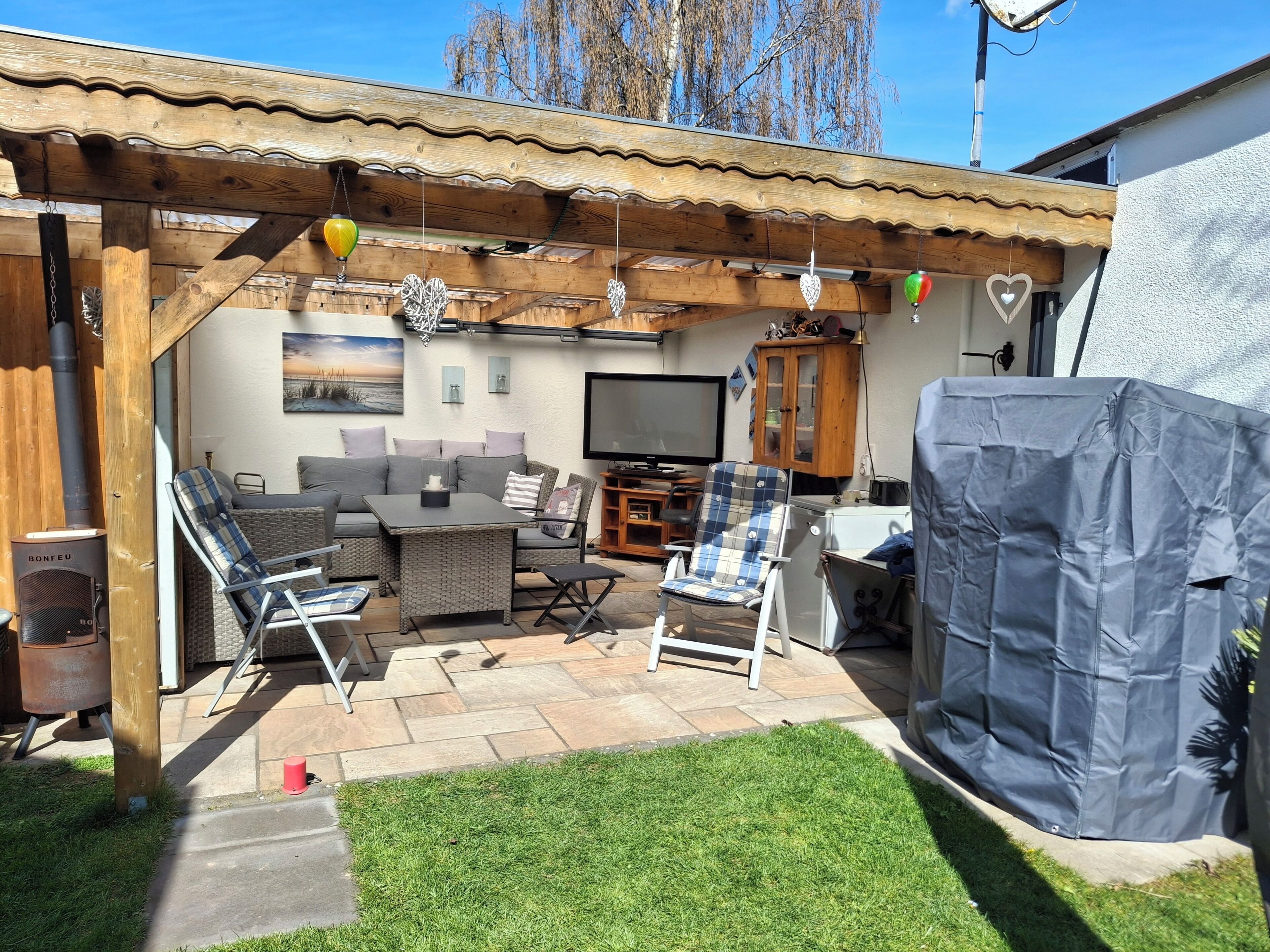 Un patio con sofá, sillas, una mesa, televisor y chimenea.