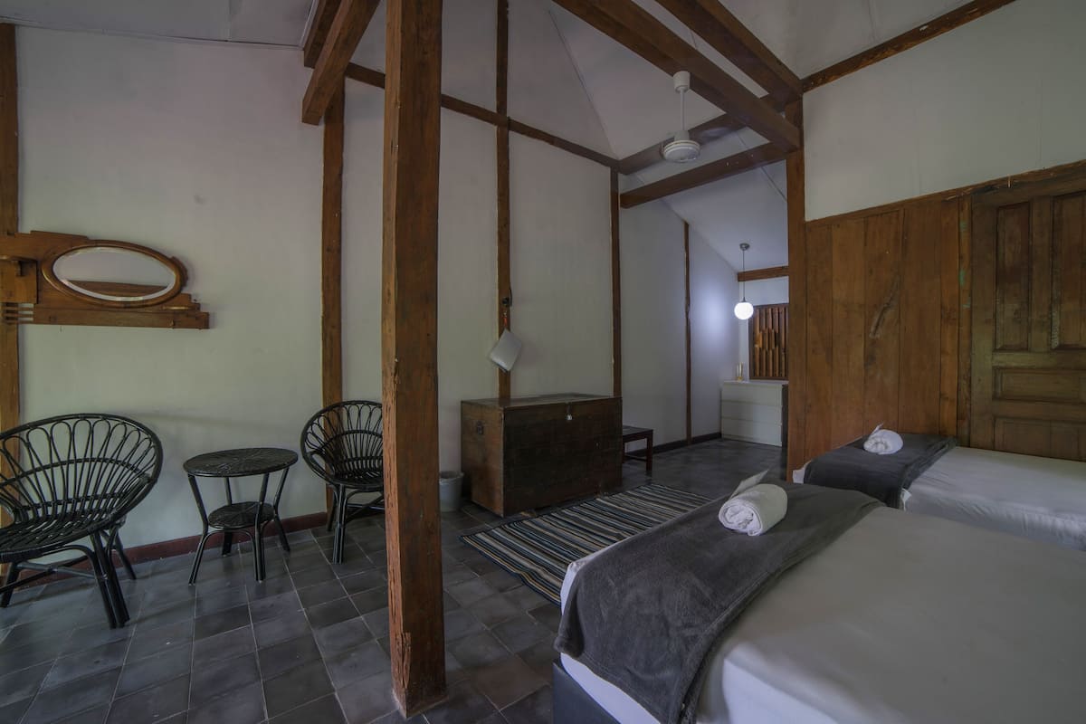 A room with a bed, two chairs, a small table, a wooden dresser, and a mirror on the wall.