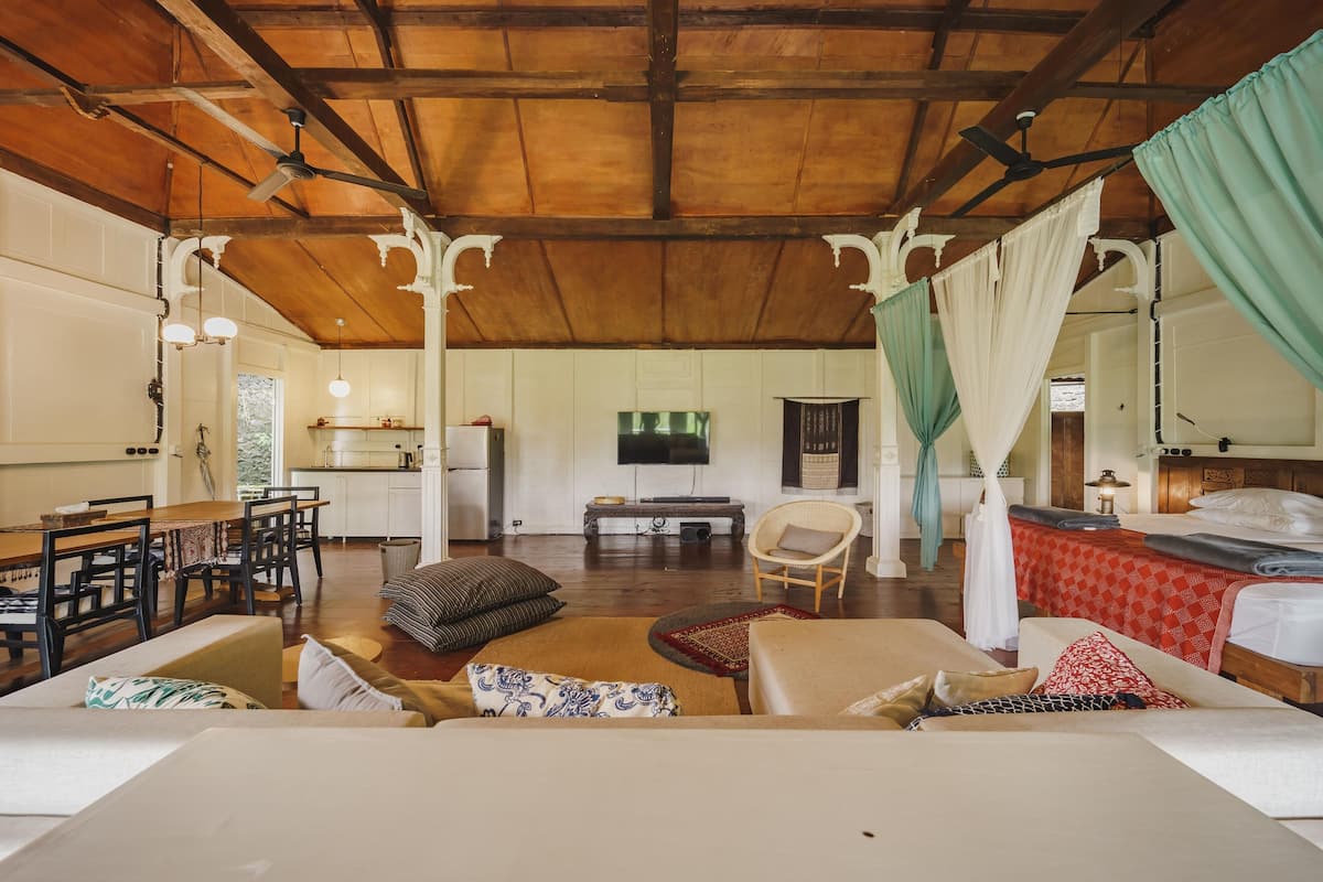 A spacious room with a wooden ceiling, a dining area with a table and chairs, a bed with a canopy, and a television mounted on the wall.