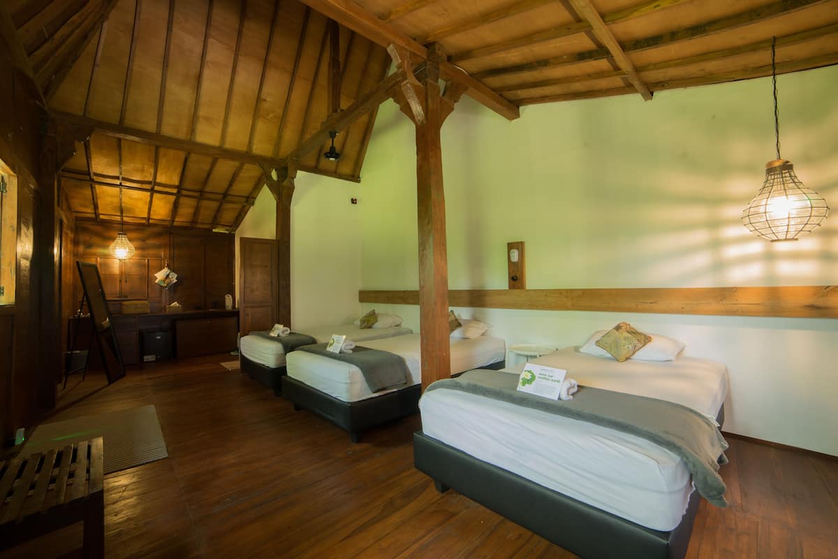A room with wooden floors and a sloped ceiling, featuring three beds with white linens and pillows, a small desk, and a hanging light fixture.