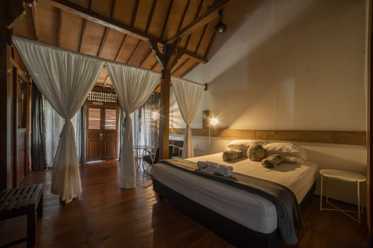 A bedroom with a wooden ceiling, a bed with pillows and a blanket, a bedside table, and a bench.