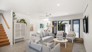 Una sala de estar moderna con un sofá gris, sillones blancos, una mesa de centro y una escalera.