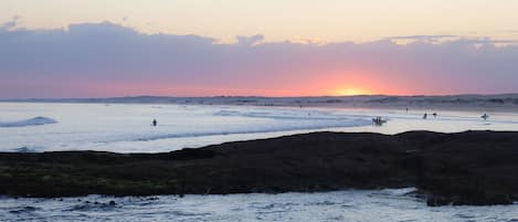 A beach scene with a sunset, rocky shoreline, and people in the water.