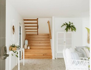 A staircase with wooden steps leading to a landing, a white door, and a white cabinet with a plant on top. - REEF Luxury Home, Ocean View, Large Pool & Hot Spa (Anna Bay)