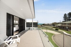 A balcony with a bed and a chair, overlooking a residential area and the ocean. - REEF Luxury Home, Ocean View, Large Pool & Hot Spa (Anna Bay)