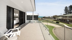 Un balcón con una cama y una silla, con vistas a una zona residencial y al océano.