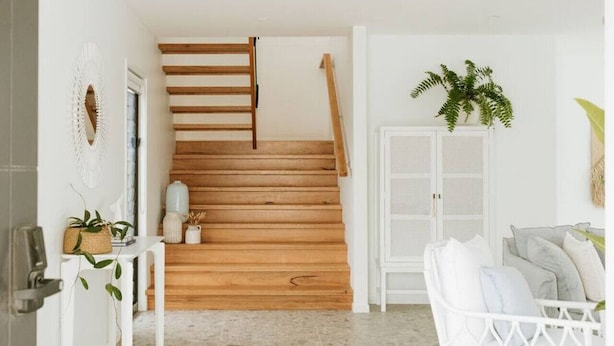 Una escalera de madera con peldaños que conduce a una plataforma, una puerta blanca y un armario blanco con una planta encima.