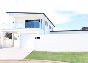 Une maison moderne à deux étages, avec une façade blanche et des touches de bleu, dotée d’une allée couverte et d’une pelouse bien entretenue.