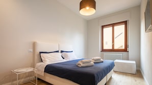 A bedroom with a bed, a bedside table, a window, and a radiator. - Ponte Vecchio White by Mmega (Florence)