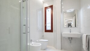A modern bathroom with a glass shower enclosure, a bidet, a toilet, and a sink with a mirror above it. - Ponte Vecchio White by Mmega (Florence)