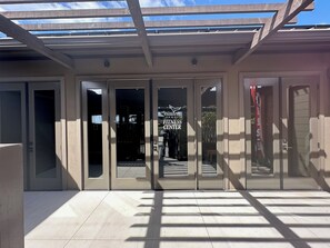 A building entrance with a glass door, a sign for 'Wailea Fitness Center,' and a covered walkway.