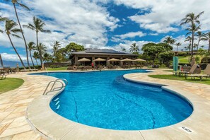 Una piscina de diseño curvo, rodeada de palmeras y un edificio con terraza.