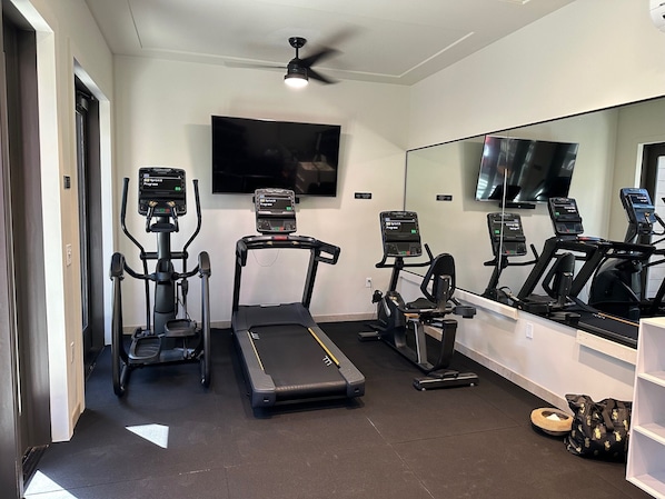Un gimnasio en casa con cintas de correr, elípticas y una bicicleta estática, equipado con monitores digitales de fitness.