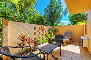 A patio with two chairs and a table, surrounded by lush greenery and a textured wall.