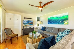 A living room with a ceiling fan, a sofa, a chair, a coffee table, and a painting on the wall.