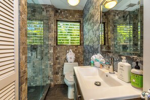 Un baño con ducha de vidrio, inodoro y lavamanos con artículos de aseo.
