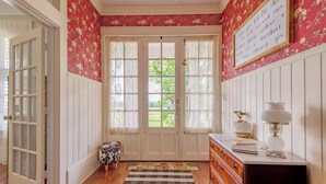 Una habitación con piso de madera, un aparador blanco, una lámpara, un taburete con estampado de vaca y una alfombra.