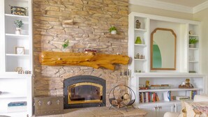Una sala de estar con chimenea de piedra, estanterías blancas y una mesa de centro de madera.