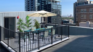 A rooftop patio with a table and chairs, surrounded by a black metal railing.
