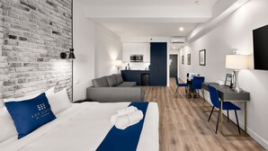 A hotel room with a bed, a sofa, a desk, a chair, a small kitchenette, and a brick wall. - Theater Lofts | Quebec, 606 (Québec City)