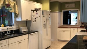 A kitchen with white cabinets, a white refrigerator, a dishwasher, and a black countertop. - Quaint Home With Dock on Lagoon - Walk to Beach (Hilton Head Island)