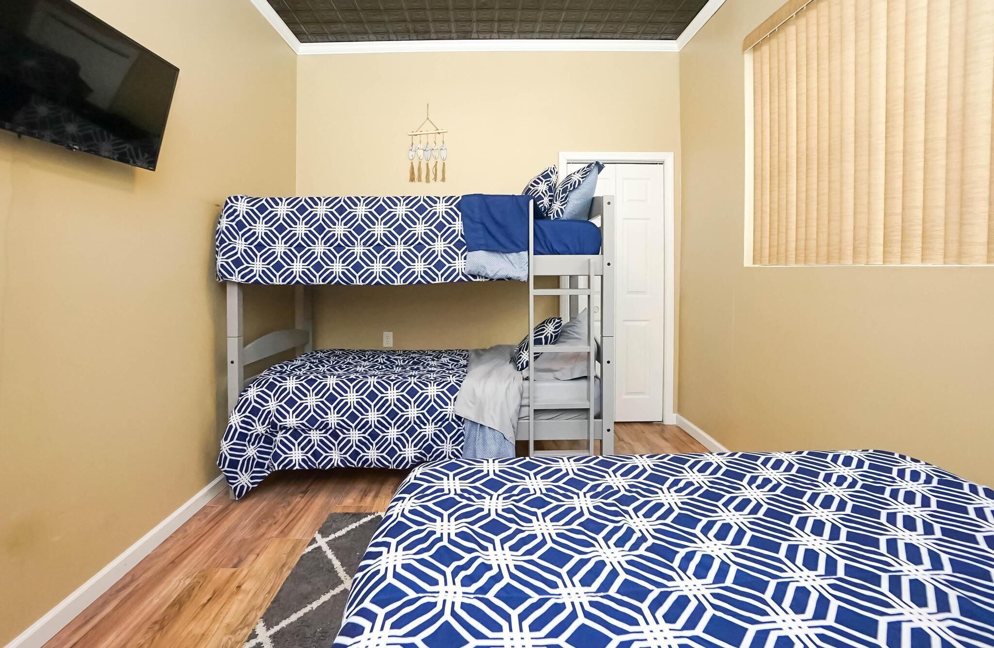 Un dormitorio con literas, suelo de madera, una puerta y una ventana con persianas.