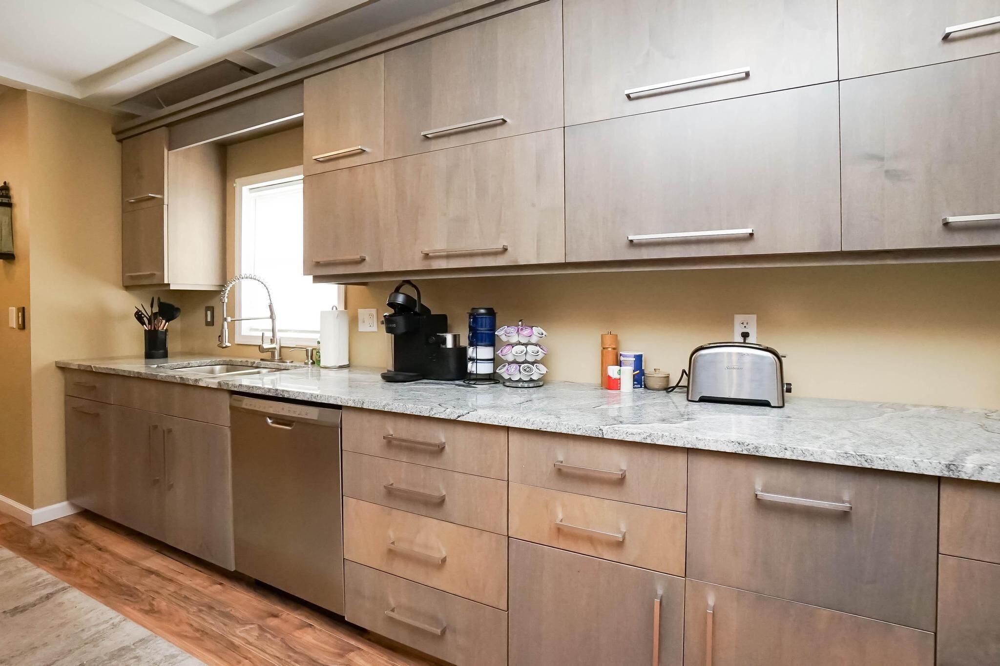 Cozinha moderna com armários de madeira, bancada de granito e diversos eletrodomésticos, incluindo cafeteira, torradeira e chaleira.