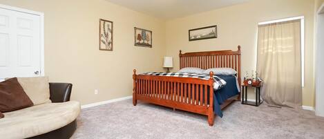 A bedroom with a bed, a chair, a ceiling fan, and a window with curtains.