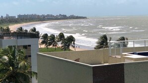 Une vue sur la côte, avec une plage, des palmiers et une silhouette urbaine en arrière-plan.