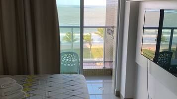 Quarto de hotel com cama, vista para o oceano e varanda com uma cadeira.