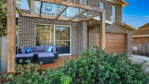 A modern house with a brick exterior, large windows, and a wooden deck with outdoor furniture. - Blissful Bungalow - a luxurious escape (Culburra Beach)