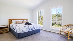 A bedroom with a bed, two windows, a chair, and a nightstand. - Blissful Bungalow - a luxurious escape (Culburra Beach)