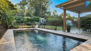 A swimming pool with a surrounding deck, a covered seating area, and a fenced garden. - Blissful Bungalow - a luxurious escape (Culburra Beach)