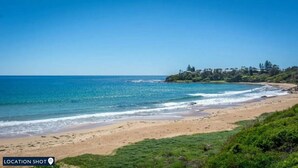 A beach with clear blue water, sandy shore, and greenery. - Blissful Bungalow - a luxurious escape (Culburra Beach)