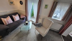 A living room with a sofa, armchair, coffee table, and a window with curtains.