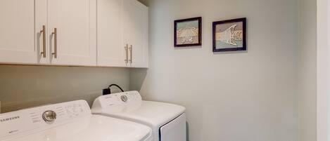 A laundry area with two white washers and dryers, a white laundry basket, and two framed pictures on the wall.