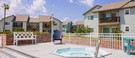 A pool area with a hot tub, wooden deck, and a white fence.