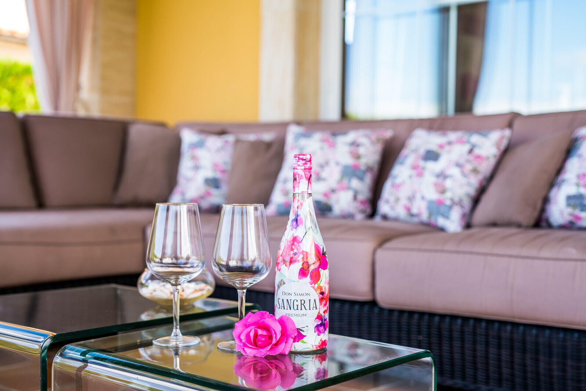 Een glazen tafel met twee wijnglazen en een fles Don Simon Sangria Premium erop.
