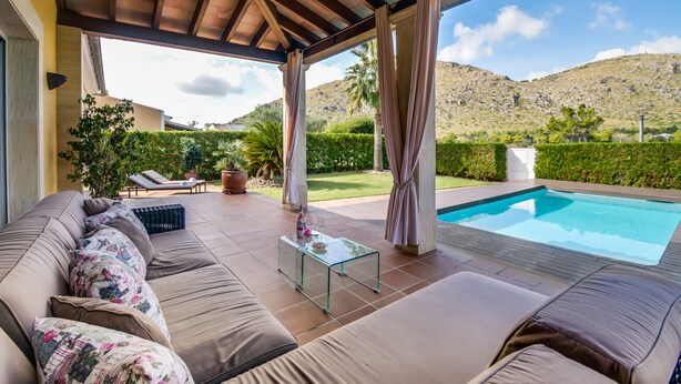 Un espace extérieur abrité avec des sièges, une piscine, des coussins de couleur beige et une table en verre.